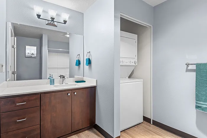 Modern bathroom with stylish vanity, ample counter space, and in-unit washer and dryer, accented by sleek lighting and vibrant decor.