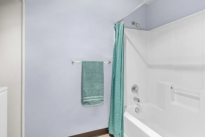 Bright and modern bathroom featuring a sleek white bathtub, elegant fixtures, and a stylish teal towel set for a refreshing ambiance.