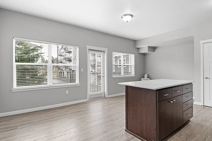 Bright open living space featuring sleek hardwood floors, modern lighting, and a stylish kitchen island with dark wood cabinetry.