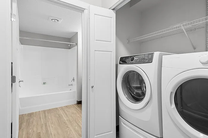 Modern bathroom and laundry area with sleek washer and dryer, featuring elegant wood flooring and bright ambiance.