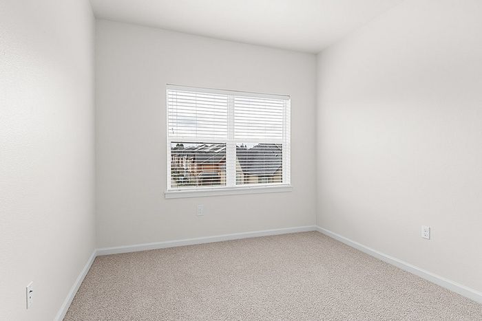 Bright and inviting bedroom with soft carpet flooring and a large window offering serene neighborhood views.