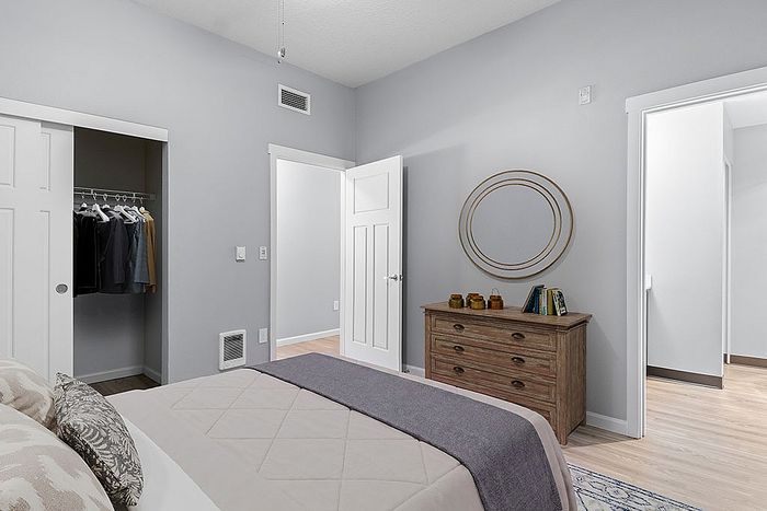 Elegant bedroom with a cozy bed, stylish dresser, and spacious closet featuring hanging clothes, perfect for modern living.