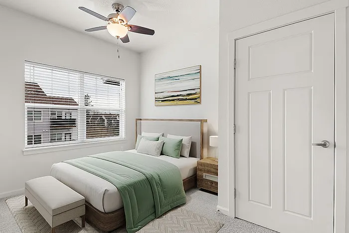 Cozy and elegant bedroom with a plush bed, modern ceiling fan, large window offering natural light, minimalist decor, and tasteful artwork.