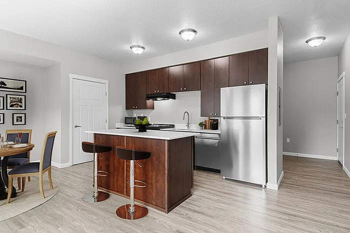 Modern apartment kitchen with sleek cherry wood cabinets, stainless steel appliances, and an inviting breakfast bar next to a cozy dining area featuring elegant framed artwork.