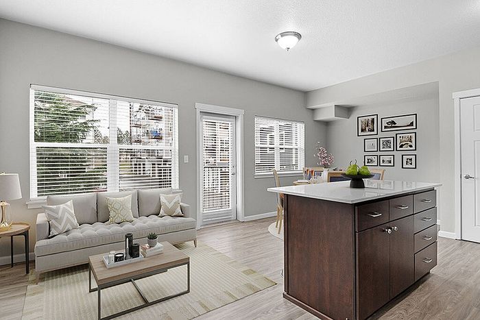 Bright and modern living room with large windows, cozy sofa, and sleek kitchen island, perfect for stylish apartment living.