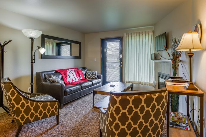 Cozy living room with stylish decor, featuring a comfortable leather sofa, patterned chairs, elegant lighting, and a wall-mounted TV, perfect for relaxation.