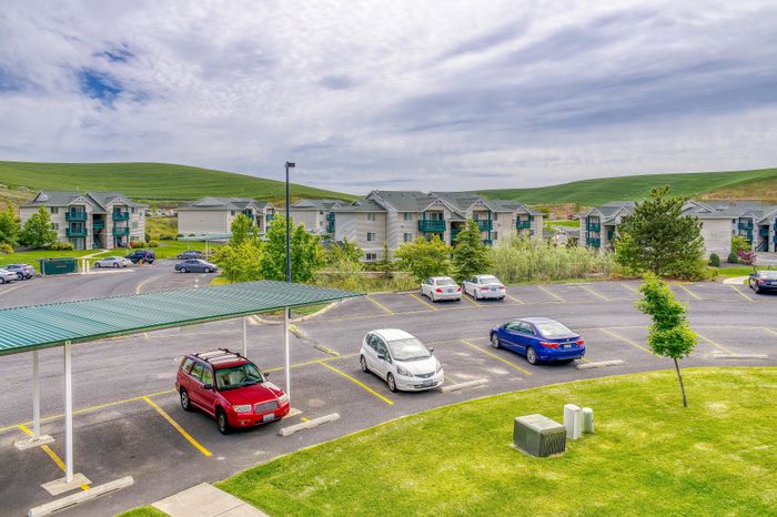 Scenic apartment complex with modern architecture, ample parking, and lush green surroundings.