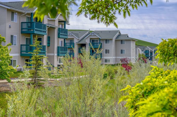 Charming apartment complex with vibrant balconies, surrounded by lush greenery and scenic landscape views.