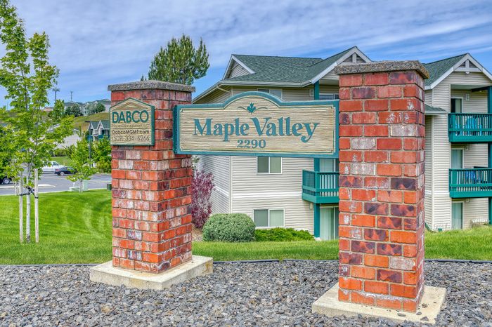 Welcoming Maple Valley sign with vibrant brick pillars, lush green surroundings, and modern apartment buildings in the background.