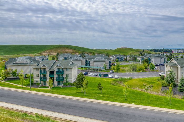 Charming apartment community set against lush green hills, featuring well-maintained buildings with balconies and spacious parking, ideal for serene living.