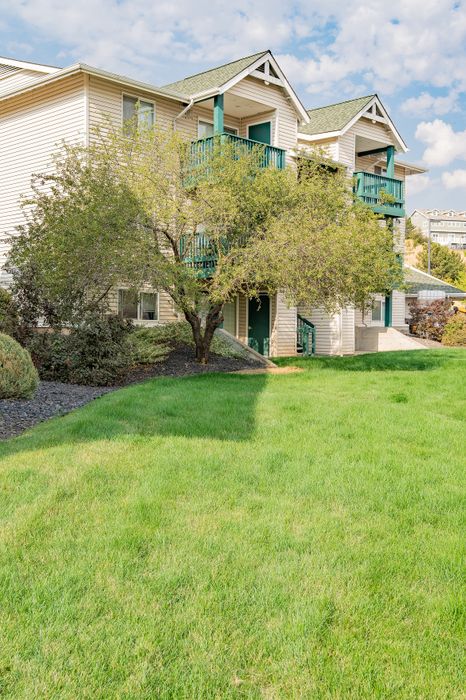 Charming apartment building with vibrant green lawns and inviting balconies, set under a beautiful blue sky.