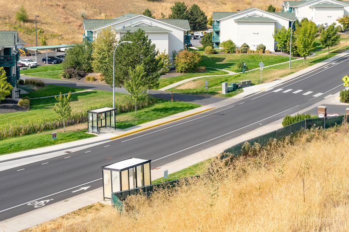 Charming suburban neighborhood view featuring modern apartment buildings, lush green lawns, and convenient bus stops along a quiet street.