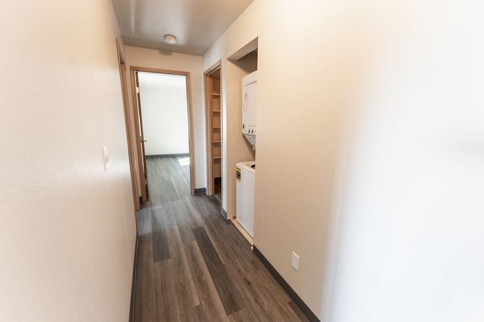 Inviting hallway with elegant wood-style flooring and in-unit laundry area, leading to a light-filled room, ideal for modern living.