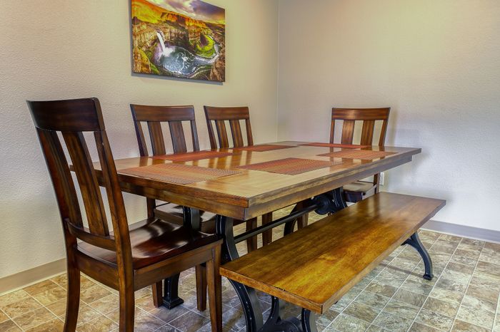 Elegant dining area with a wooden table, four chairs, and a bench, adorned with vibrant artwork and tile flooring.