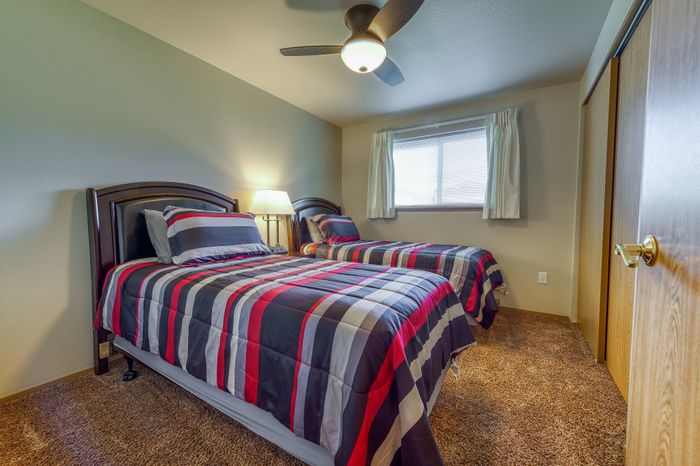 Inviting bedroom with double beds adorned in vibrant striped comforters, featuring a cozy carpet and a ceiling fan for comfort.