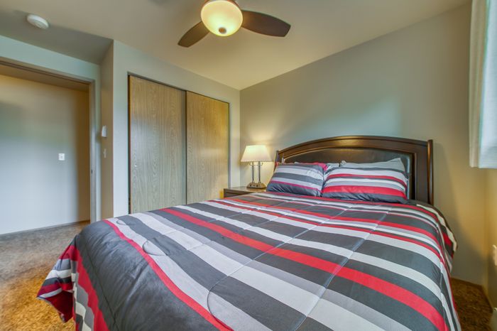 Inviting bedroom with a cozy queen bed featuring vibrant striped bedding, modern ceiling fan, and warm ambient lighting.