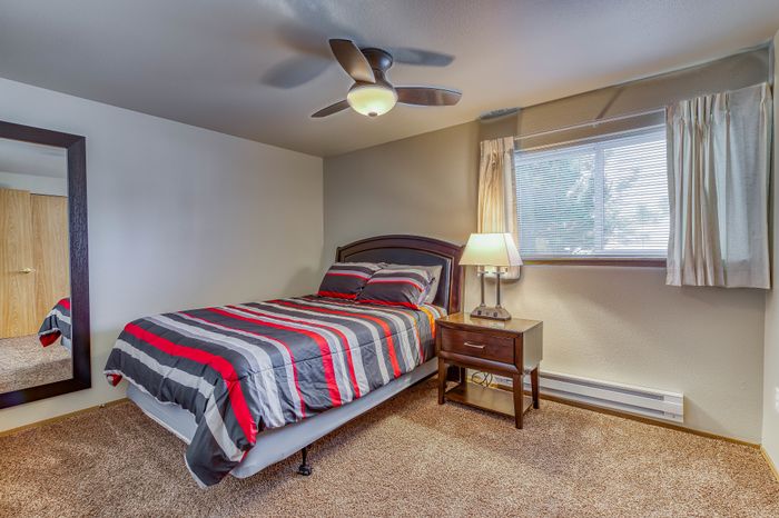 Cozy bedroom featuring a comfortable bed with stylish striped bedding, a modern ceiling fan, and natural light streaming through the window.