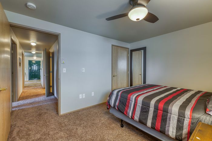 Inviting bedroom with modern ceiling fan, chic striped bedding, and a view of the cozy carpeted hallway.