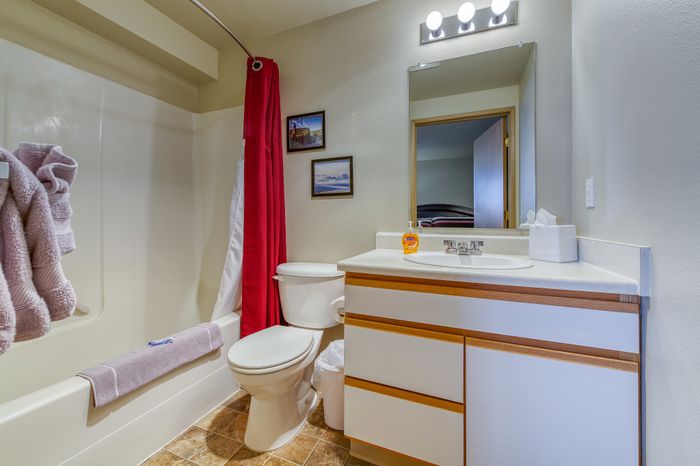 Inviting bathroom with modern fixtures, featuring a sleek vanity, classic shower-tub combo, and vibrant red shower curtain accented by cozy towels.