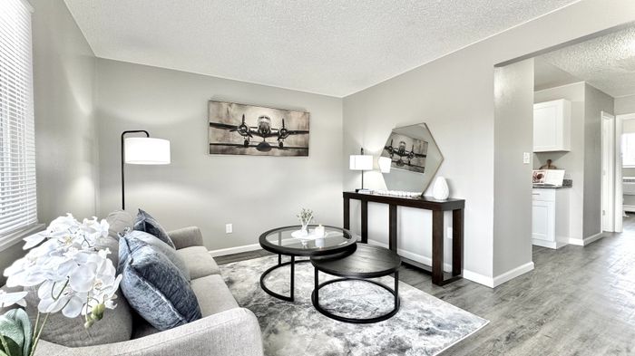 Inviting living room with modern decor, cozy gray sofa, stylish coffee table, and elegant lighting, leading to a bright kitchen area.