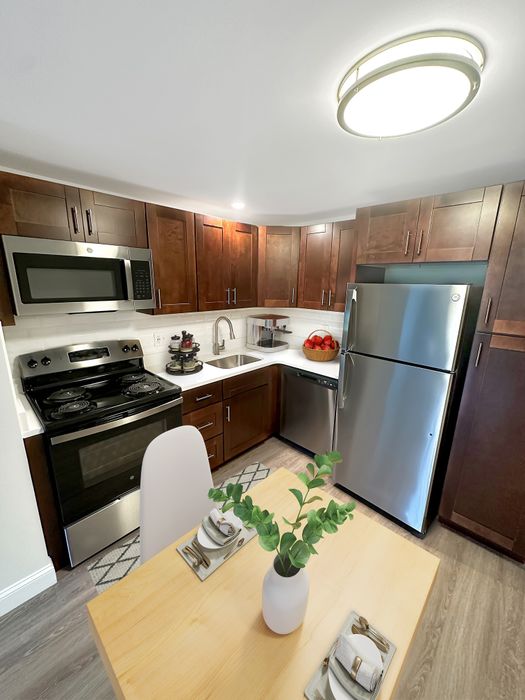 Modern kitchen with stainless steel appliances, wood cabinetry, and dining area in a staged apartment at Westgate Arms in Salem, New Hampshire