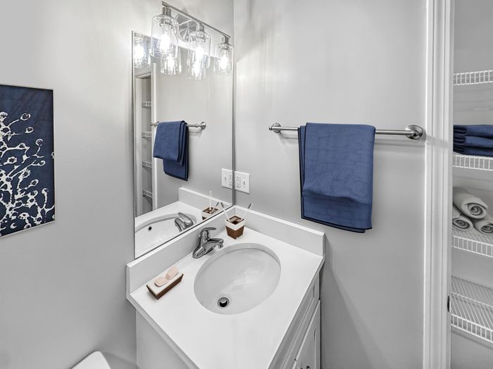 Bathroom with modern vanity, large mirror, bright lighting, and built-in storage shelving at Westgate Arms in Salem, New Hampshire