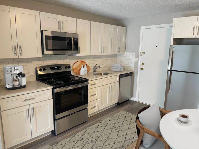 Updated apartment kitchen with light cabinetry, stainless steel appliances, tile backsplash, and wood-style flooring