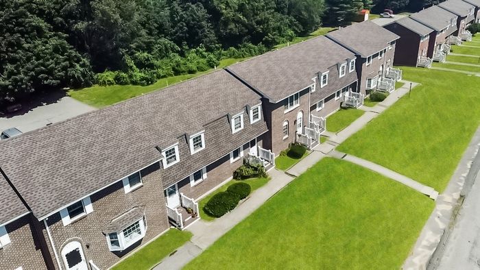 Aerial view of Meadowbrook Village brick townhomes with private entrances and landscaped lawns in Gardner, MA.