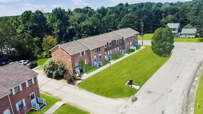 Aerial view of Meadowbrook Village townhomes beside an open green lawn in Gardner, MA