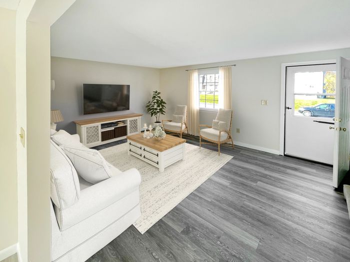 Living room with large window, private exterior entry door, and wood-style flooring at Meadowbrook Village in Gardner, Massachusetts