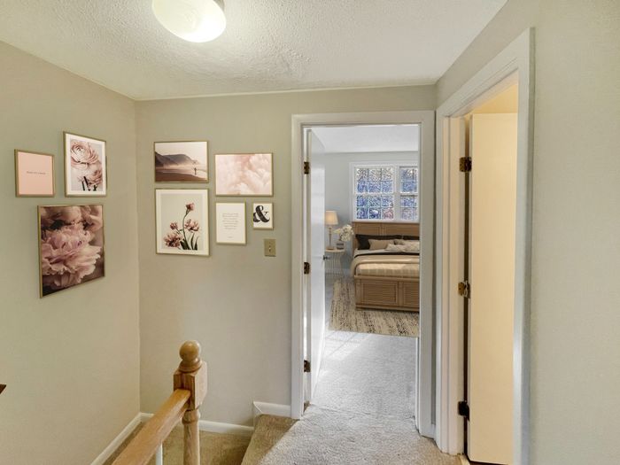 Carpeted upstairs hallway with wall decor and doorway leading to bedroom at Meadowbrook Village in Gardner, Massachusetts
