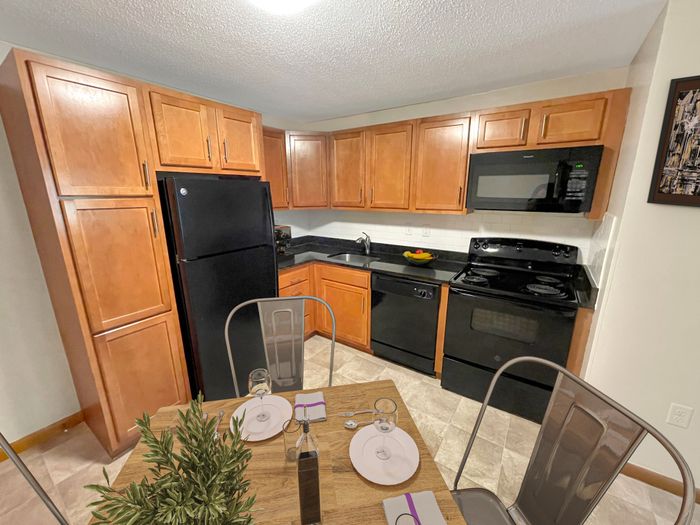 Apartment kitchen with wood cabinetry, black appliances, and tile flooring at Woodlands at Nashua