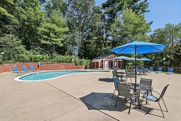 Outdoor pool and shaded patio seating at Woodlands at Nashua apartment community in Nashua, NH