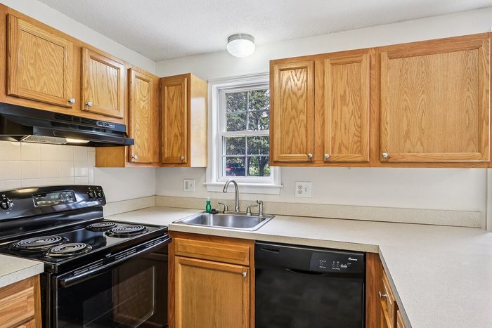 Meadowbrook Village kitchen with a window above the sink, wood cabinets, and a black dishwasher and range.