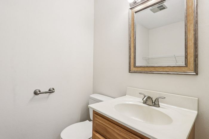 Meadowbrook Village half bathroom with a wood vanity, sink, framed mirror, and toilet.