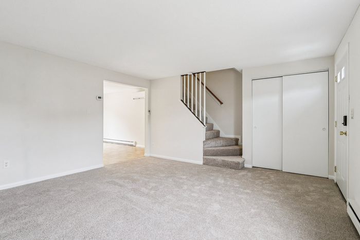 Unfurnished Meadowbrook Village living room with carpet, an entry closet, and stairs leading upstairs.