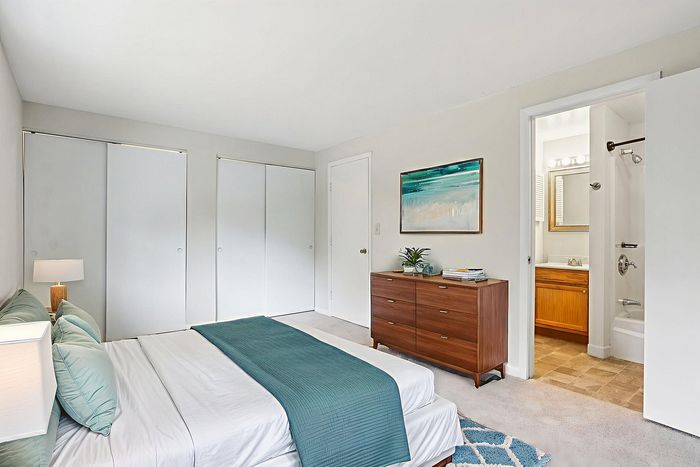 Virtually staged Meadowbrook Village bedroom showing a bed, dresser, closet doors, and adjoining bathroom.