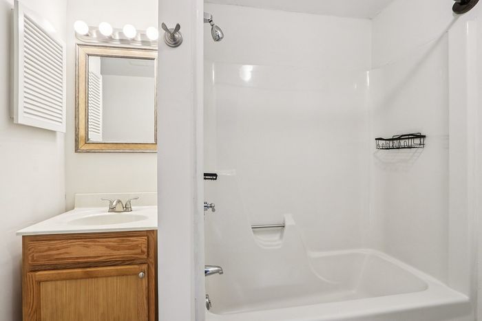Meadowbrook Village bathroom with a wood vanity, framed mirror, and bathtub with shower.