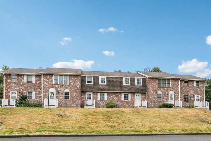 Front view of Meadowbrook Village brick townhomes with individual entrances and a shared lawn in Gardner, MA.
