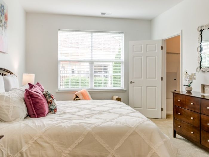One Bedroom Garden Style Apartments in Mt. Laurel Township NJ - Laurel Green - Furnished Bedroom with a Large Bed, Carpeted Flooring, Wooden Dresser, Cushioned Bench, White Walls, and a Large Window