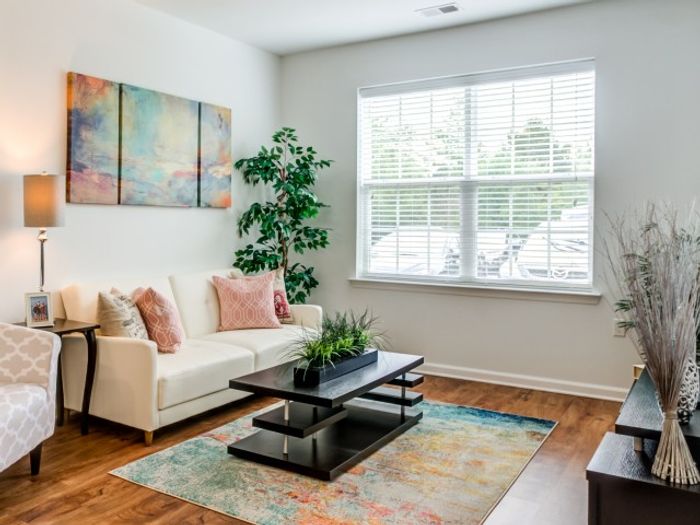 Garden Style Apartments in Mt. Laurel Township NJ - Laurel Green - Spacious Living Room with White Sofa, Wood-Style Flooring, Multi-Leveled Coffee Table, Colorful Rug, Armchair, Table, White Walls, and a Window