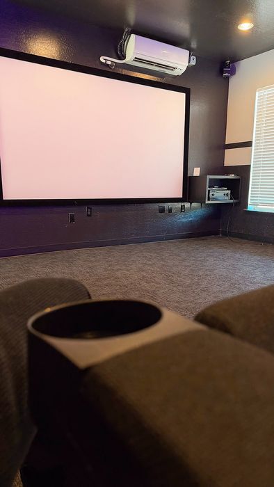 Luxurious home theater room with a large projector screen, modern sound system, and plush seating featuring a convenient cup holder.