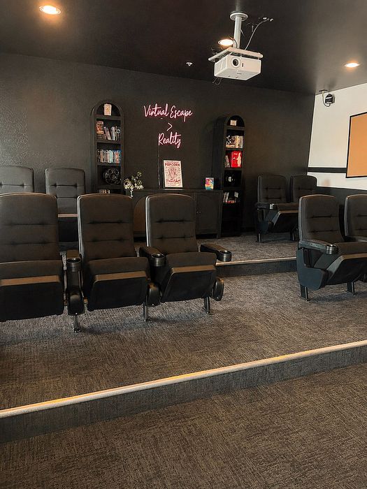Chic private cinema room featuring plush reclining seats, ambient lighting, and a stylish 'Virtual Escape to Reality' neon sign.