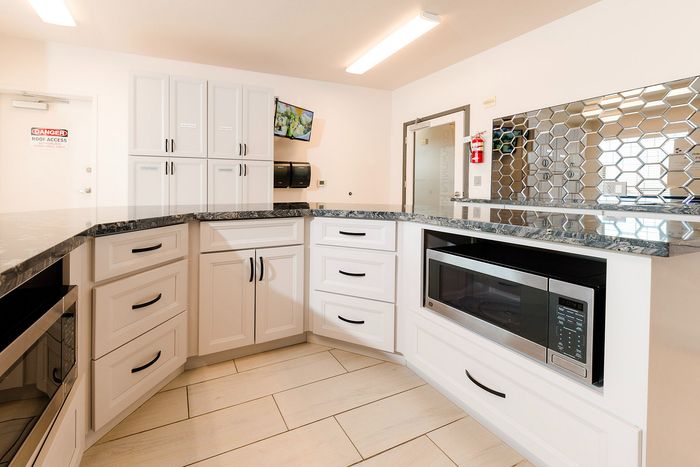 Modern kitchen with sleek white cabinetry, black marble countertops, and stainless steel appliances, featuring a stylish mirrored backsplash.