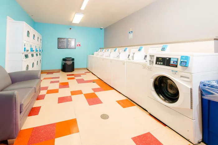 Bright and modern laundry room featuring multiple washing machines, vibrant flooring, and comfortable seating.