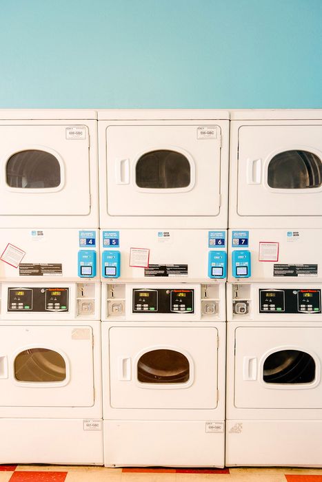 Modern laundry facility featuring six stacked front-loading washers and dryers with bright blue accents, set against a soothing light blue wall.
