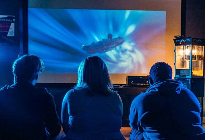 Cozy home theater with three people enjoying a movie, surrounded by ambient blue lighting, and a classic popcorn machine, creating the perfect entertainment atmosphere.