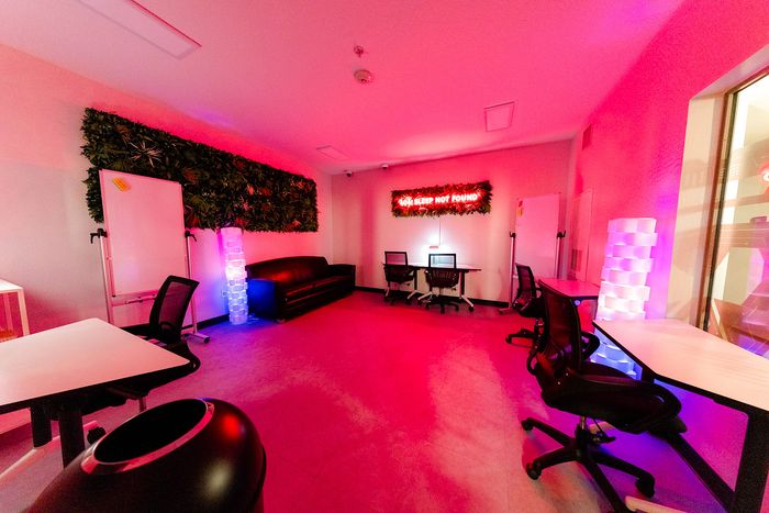 Vibrant co-working space with neon lighting, modern chairs, lush greenery, and motivational decor.