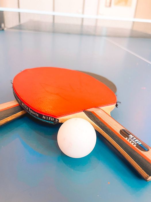 Vibrant table tennis setup with two paddles and ball on a sleek blue ping pong table.
