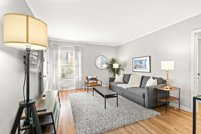 Bright and inviting living room featuring a stylish gray sofa, chic accent chair, modern floor lamp, and a plush area rug on elegant wooden flooring.